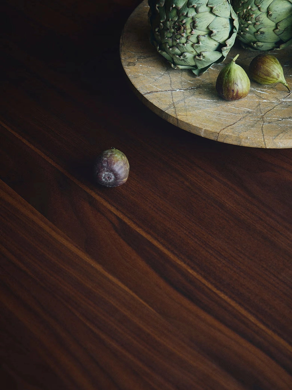 Tinted Objects Sanders Round Dining Table, showcasing a rich, dark brown wooden surface with prominent natural grain patterns. This elegant and durable dining table is perfect for modern homes seeking a sophisticated centerpiece for family meals and entertaining.