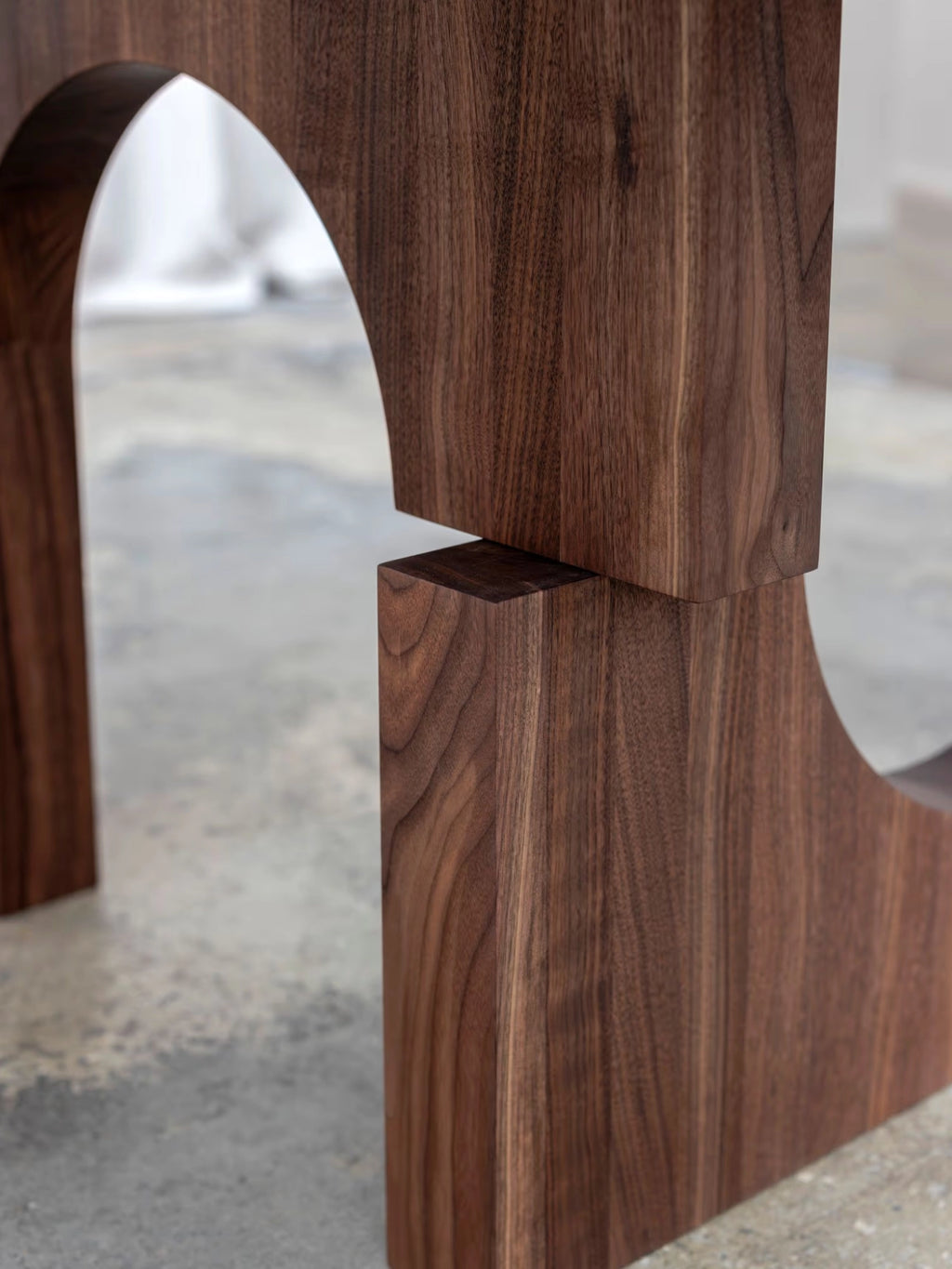 Tinted Objects Sanders Round Dining Table, featuring a close-up of its modern solid walnut wood base with rich brown grain and unique arched cutouts. This stylish dining table is perfect for contemporary homes seeking elegant and durable furniture.