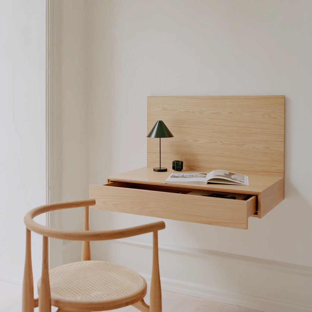 New Works Tana Wall Mounted Desk, a sleek Scandinavian floating desk crafted from light oak wood, featuring a clean rectangular back panel and a seamlessly integrated single drawer. Its natural wood grain and minimalist form offer a modern aesthetic, perfect for a space-saving home office, stylish entryway, or functional bedroom desk in contemporary interiors.