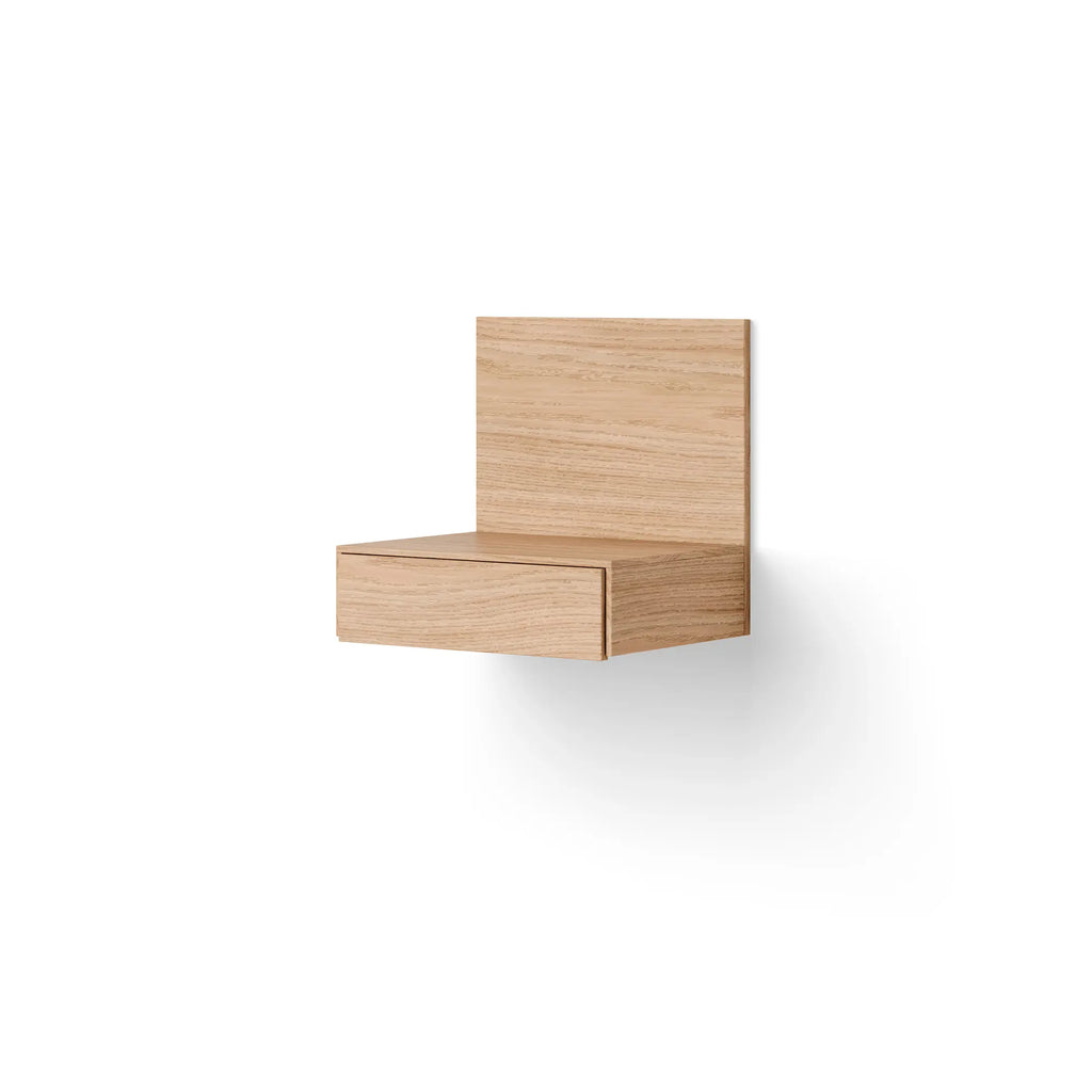 New Works Tana Wall Mounted Nightstand, a minimalist floating shelf crafted from natural solid oak wood, featuring a sleek rectangular design with a discreet integrated drawer and a tall back panel, showcasing clean Scandinavian lines and a smooth, light wood grain texture. Ideal as a contemporary bedside table for modern minimalist bedrooms or a stylish storage solution for small living spaces.