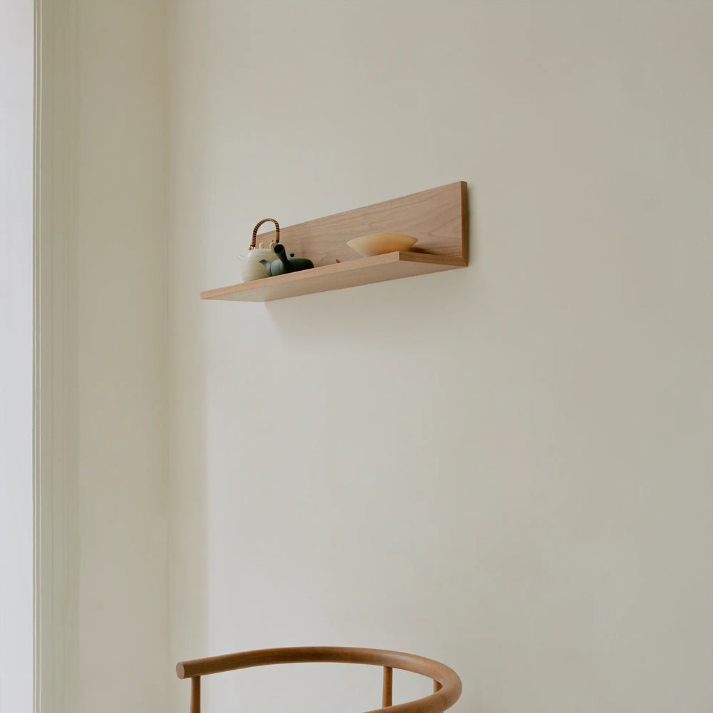 New Works Tana Wall Shelf, a modern minimalist floating shelf crafted from light natural solid oak wood, featuring a clean, elongated profile with a subtle raised back panel.