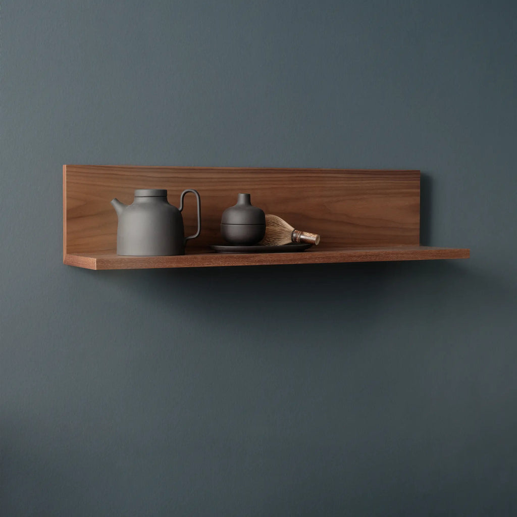 New Works Tana Wall Shelf, a modern minimalist floating wall shelf crafted from rich solid walnut wood. It features clean, architectural lines with a warm brown finish, offering a sleek display solution for contemporary interiors. Ideal for Scandinavian living rooms, bedrooms, or home offices for elegant shelf styling.
