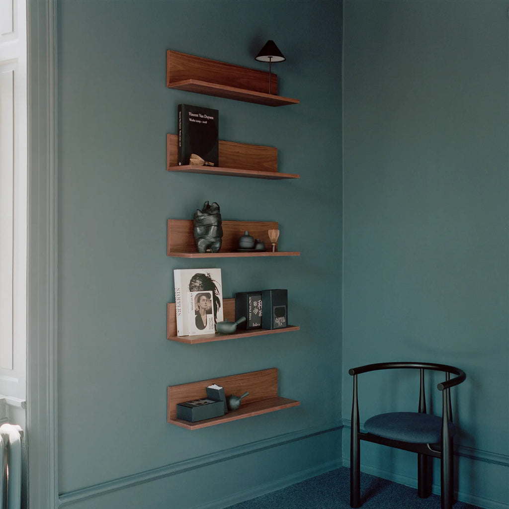 New Works Tana Wall Shelf, a modern minimalist wall shelf crafted from rich, dark solid walnut wood. It features a clean, rectangular floating design with a distinctive integrated back panel that creates a subtle ledge for displaying books and decor. Ideal for contemporary living rooms, Scandinavian bedrooms, or stylish home office shelving.