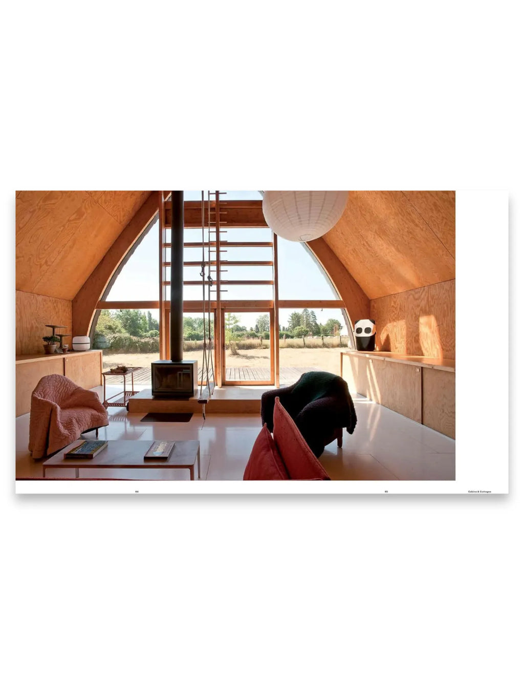 Book The Design Retreat, showcasing a modern A-frame interior with warm plywood walls and a central black wood-burning stove. This architecture and design book is perfect for enthusiasts seeking unique interior inspiration.