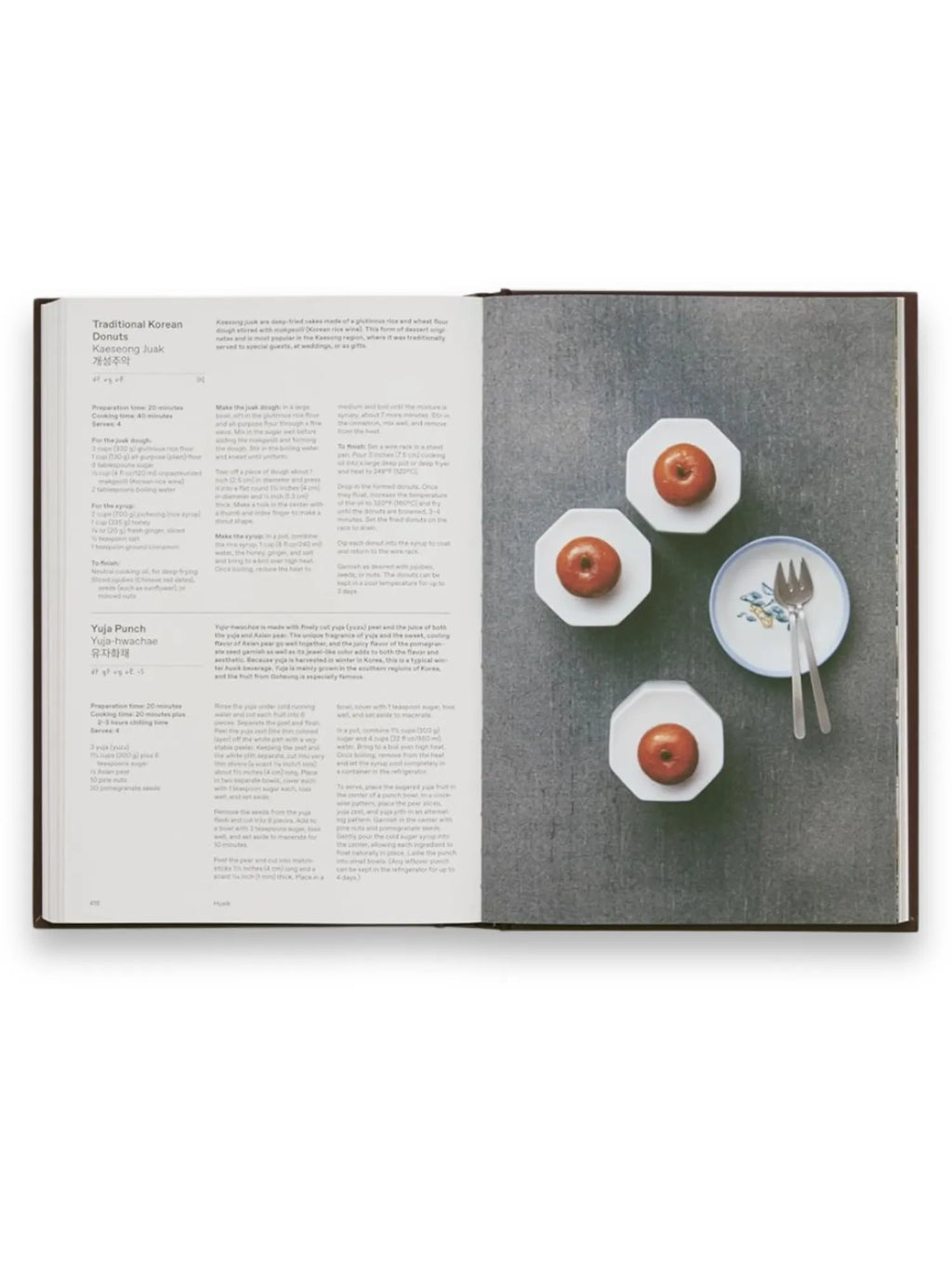 Book The Korean Cookbook, open to a recipe for "Traditional Korean Donuts" with an image displaying three small, round, golden-brown donuts on white octagonal plates, and a fourth octagonal plate with two silver forks and a small floral-patterned bowl. This premium cookbook offers delightful Korean dessert recipes for home chefs and culinary enthusiasts.