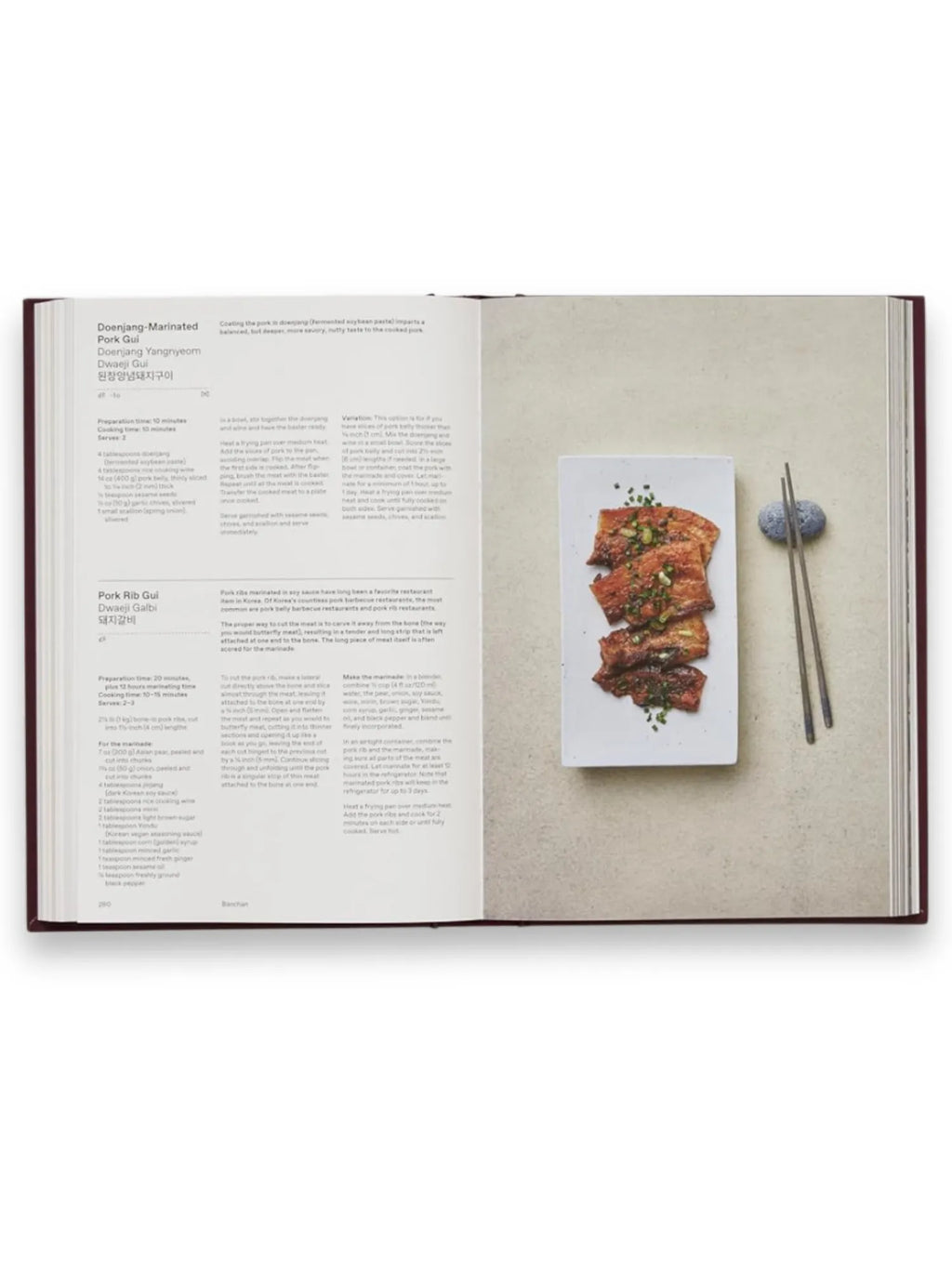 Book The Korean Cookbook, an open hardcover cookbook showcasing a detailed recipe for "Doenjang-Marinated Pork Gui" with a vibrant, high-quality photograph of the dish on a white rectangular plate next to elegant chopsticks on a stone rest. This essential culinary guide is perfect for home cooks eager to explore authentic Korean cuisine and cooking techniques.