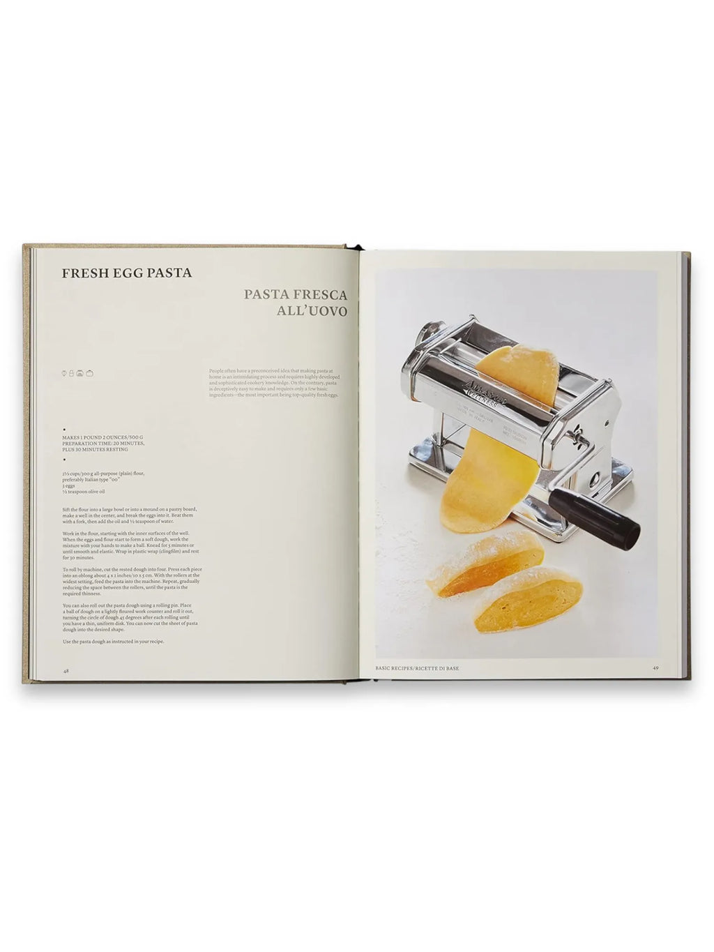 Book The Silver Spoon, open hardcover cookbook displaying a "Fresh Egg Pasta" recipe with a vibrant photo of a chrome pasta maker extruding golden dough, alongside recipe text. This classic Italian cookbook is perfect for home cooks and culinary enthusiasts seeking authentic recipes and cooking inspiration.