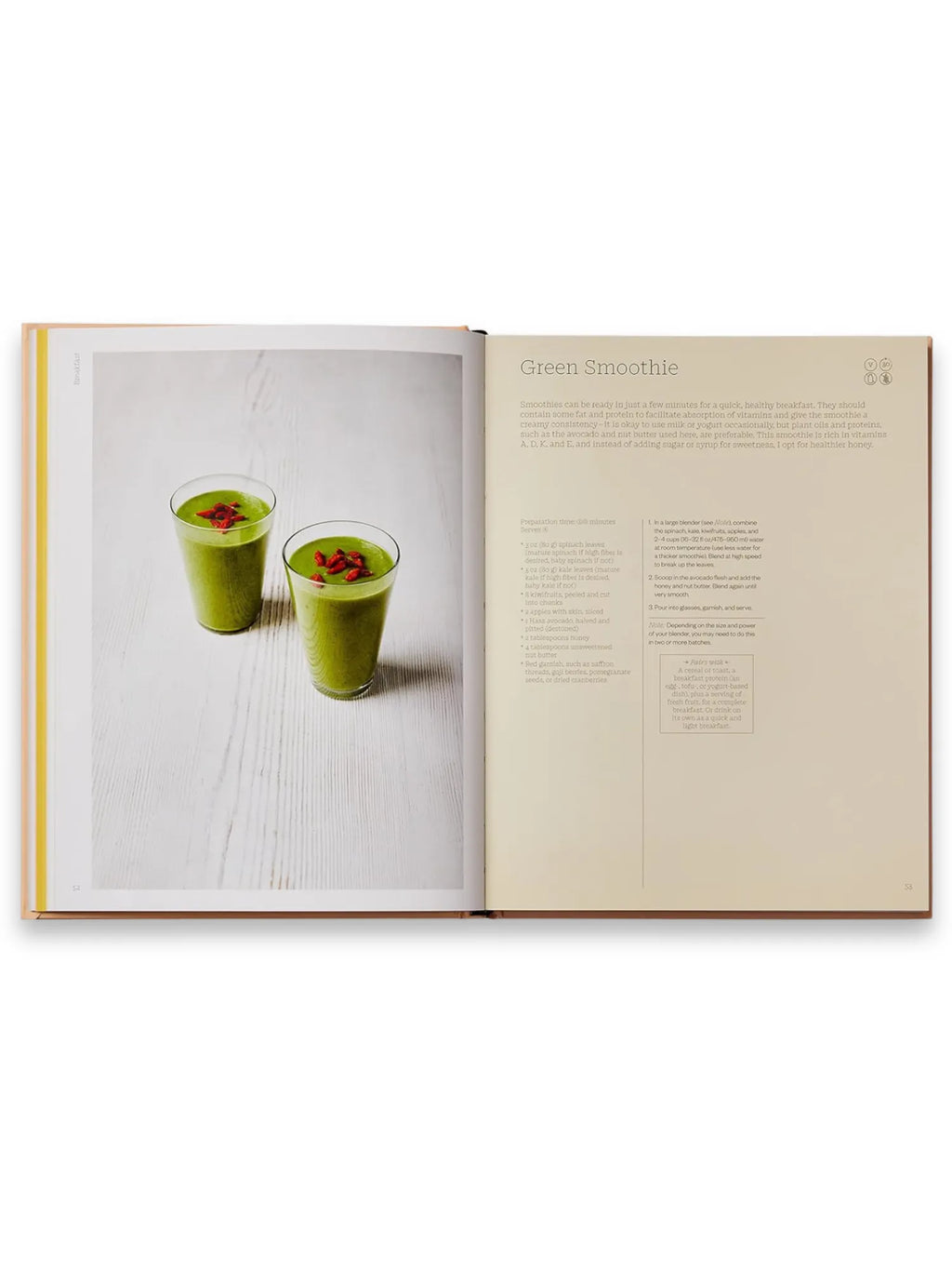 Book The Wellness Principles: Cooking for a Healthy Life, an open cookbook displaying a vibrant green smoothie recipe with two glasses of garnished smoothie on a rustic white wooden surface. This essential healthy eating guide offers nutritious recipes and culinary inspiration for health-conscious home cooks.