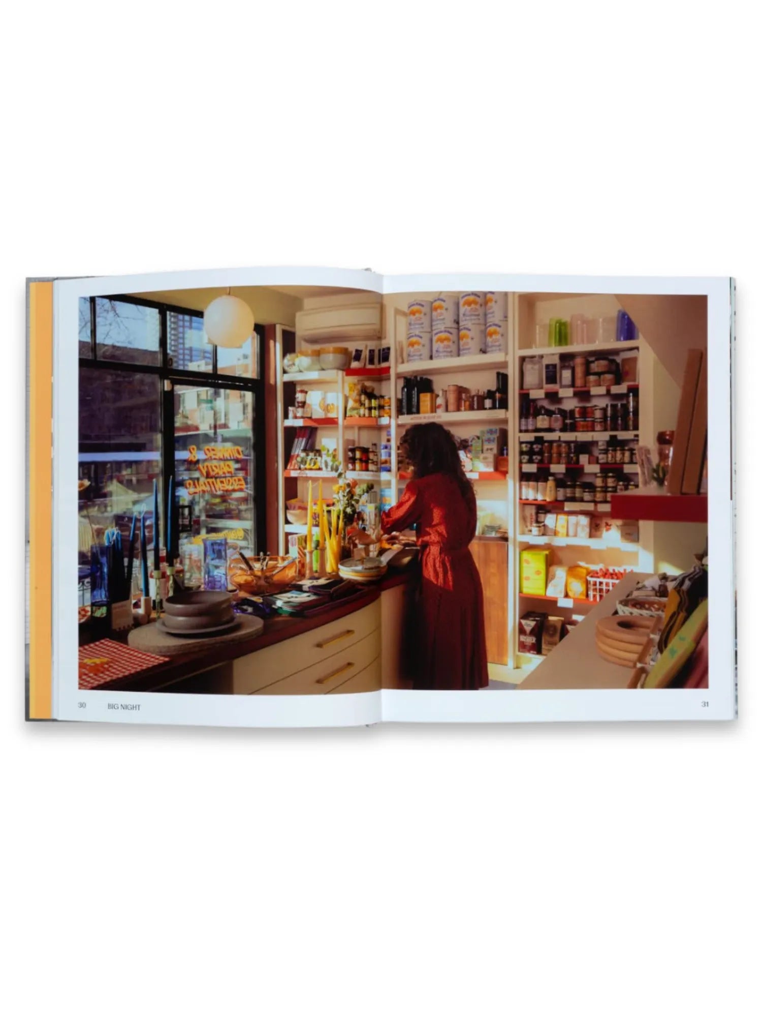 Book Think Big Shop Small, an open page spread featuring a vibrant photo of a woman in a red dress working in a cozy, well-stocked specialty food shop, showcasing various gourmet products on shelves and a counter with candles and dishes. This inspiring business book is perfect for aspiring entrepreneurs and small business owners seeking motivation and practical advice.