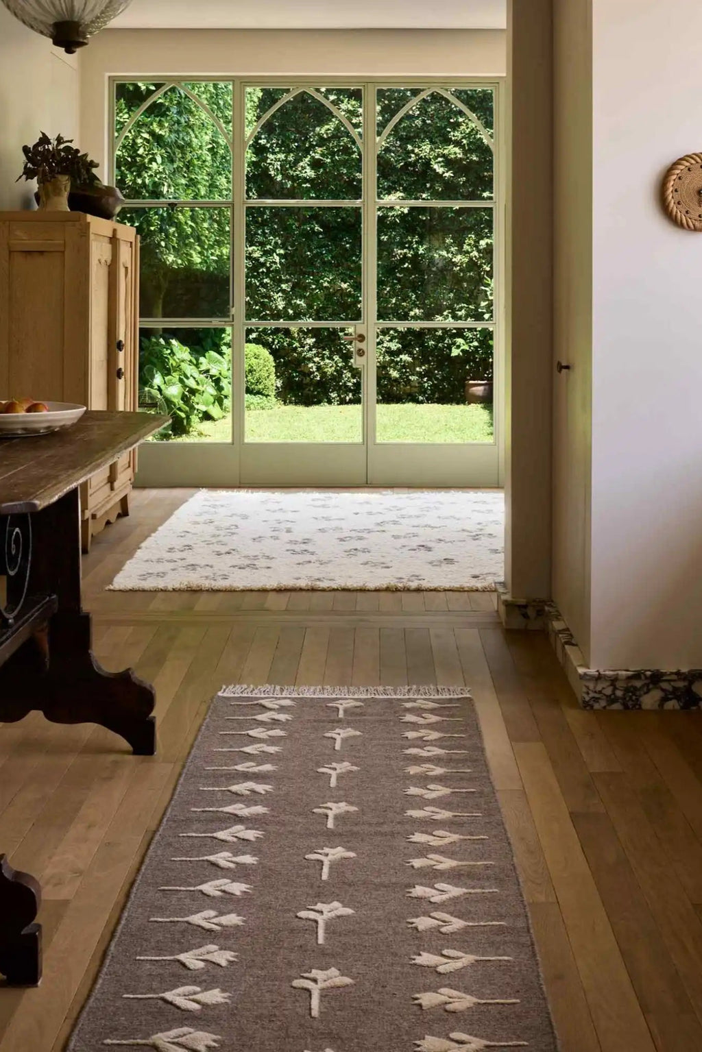 Cappelen Dimyr Colonnade No.09 Rug, a hand-knotted wool runner rug featuring a soft grey base with contrasting raised cream-colored botanical patterns arranged in two columns, finished with delicate fringe. This organic modern and rustic Mediterranean-inspired wool rug is perfect for adding texture and warmth to hallways, entryways, or living room spaces.