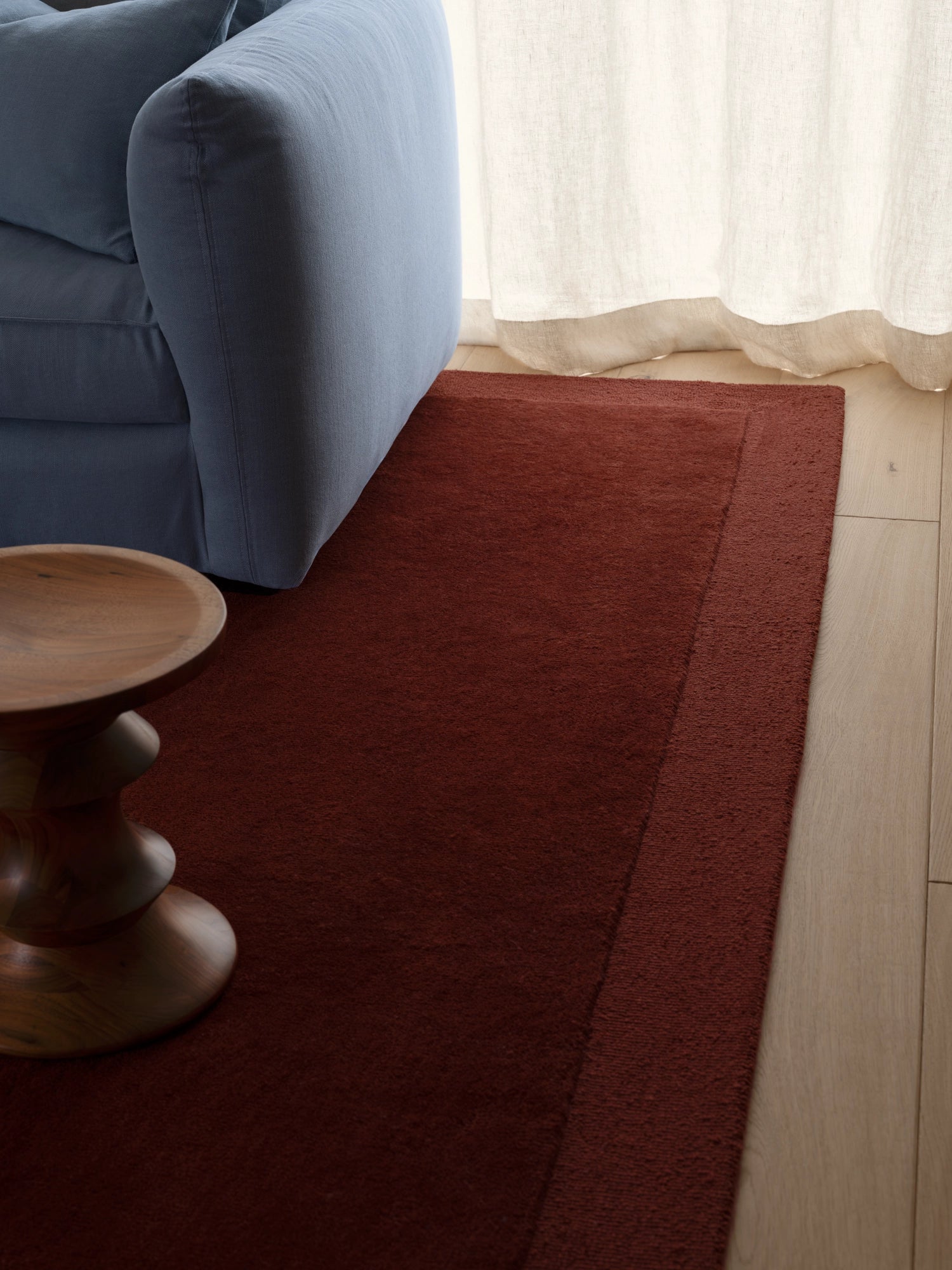 Tinted Objects Louis Wool Rug, a rectangular hand-loomed wool area rug in a rich terracotta or reddish-brown color with a plush, soft texture and a subtle tonal border. This warm contemporary rug is ideal for adding an earthy touch to modern minimalist living rooms, cozy bedrooms, or organic modern spaces.