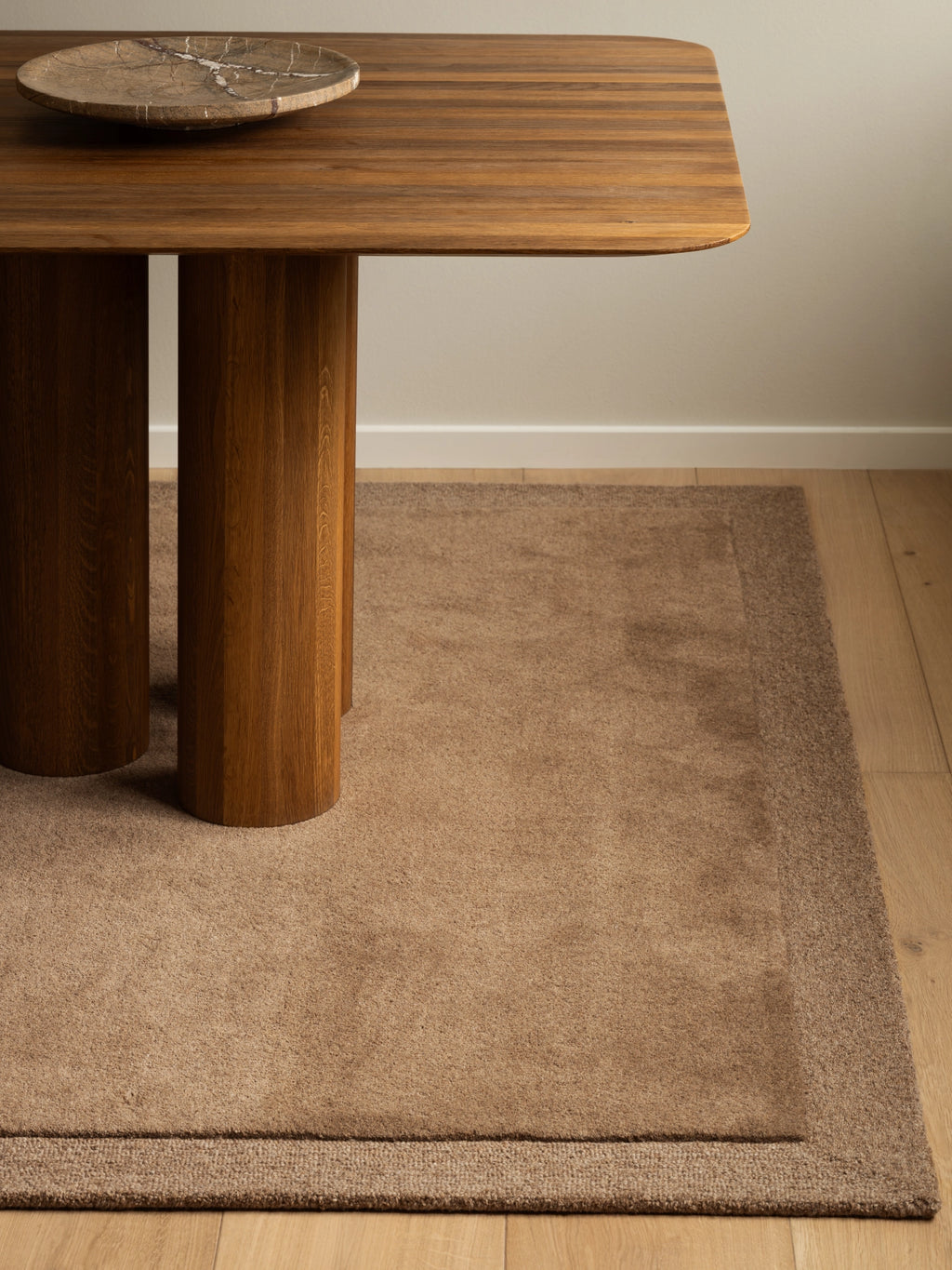 Tinted Objects Louis Wool Rug, a luxurious, neutral beige area rug with a subtle darker border, showcasing a soft, dense pile texture. This elegant wool rug is perfect for adding warmth and sophisticated style to any modern living room or dining space.