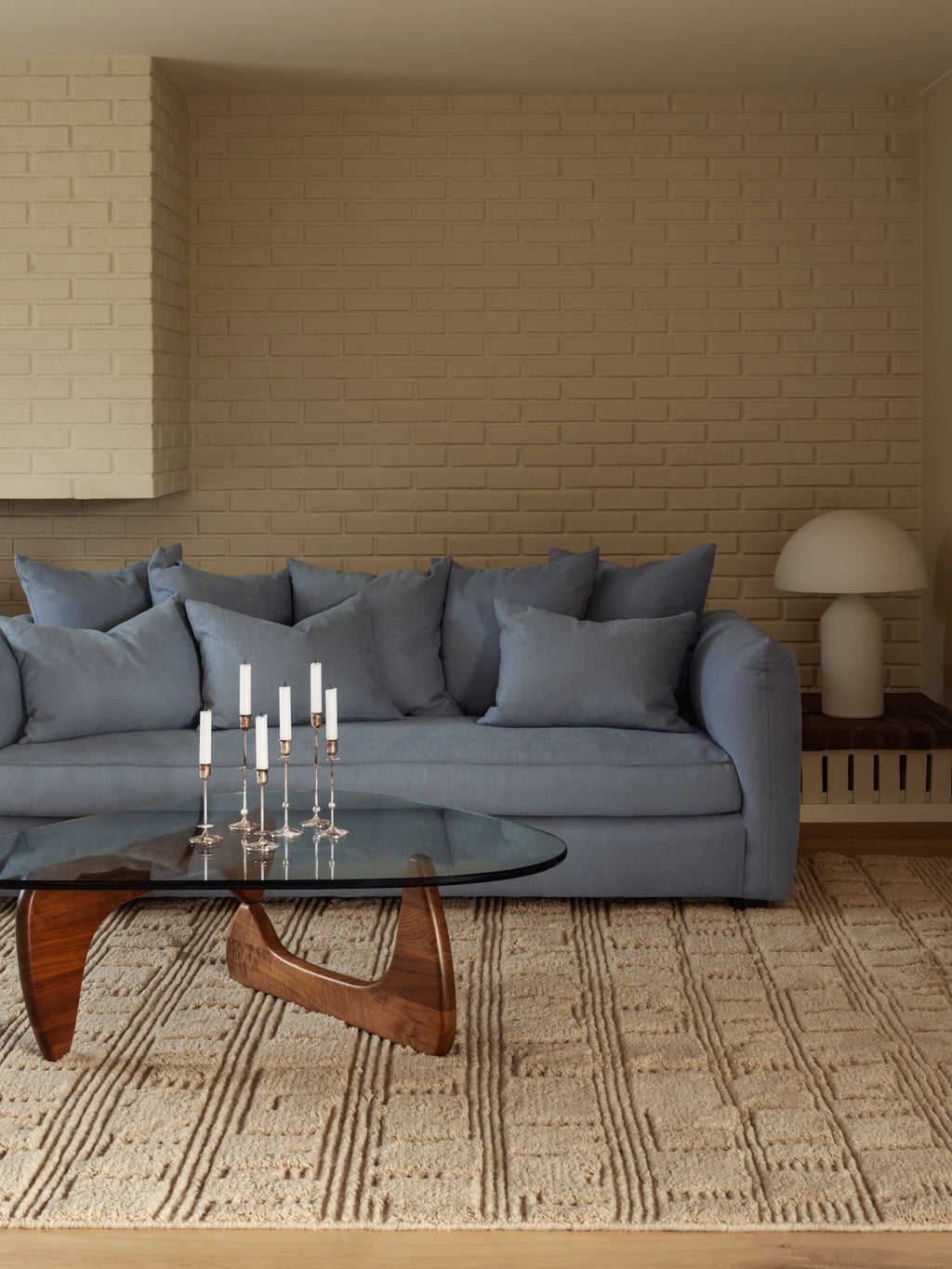 Tinted Objects Cornell Sofa, a stylish modern sofa upholstered in soft blue fabric with plush loose back cushions and armrests, paired with a glass coffee table and textured rug. This comfortable and elegant anchor piece is perfect for contemporary living rooms seeking both style and relaxation.