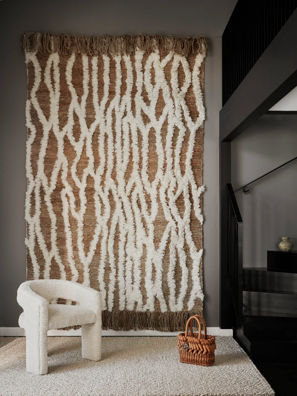 Tinted Objects Wahl Jute Rug, featuring a natural brown woven jute base with thick, textured cream-colored abstract patterns and a fringed top edge. This versatile wall hanging or area rug adds a unique, bohemian touch to modern living spaces.