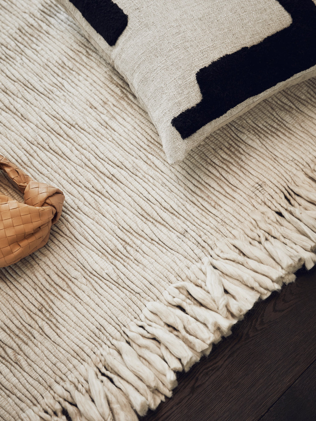 Tinted Objects Fagerlund Wool Rug, a luxurious cream-colored textured area rug with chunky fringe accents, lying on a dark wooden floor. This premium natural fiber rug is perfect for adding warmth and sophisticated texture to modern living spaces.