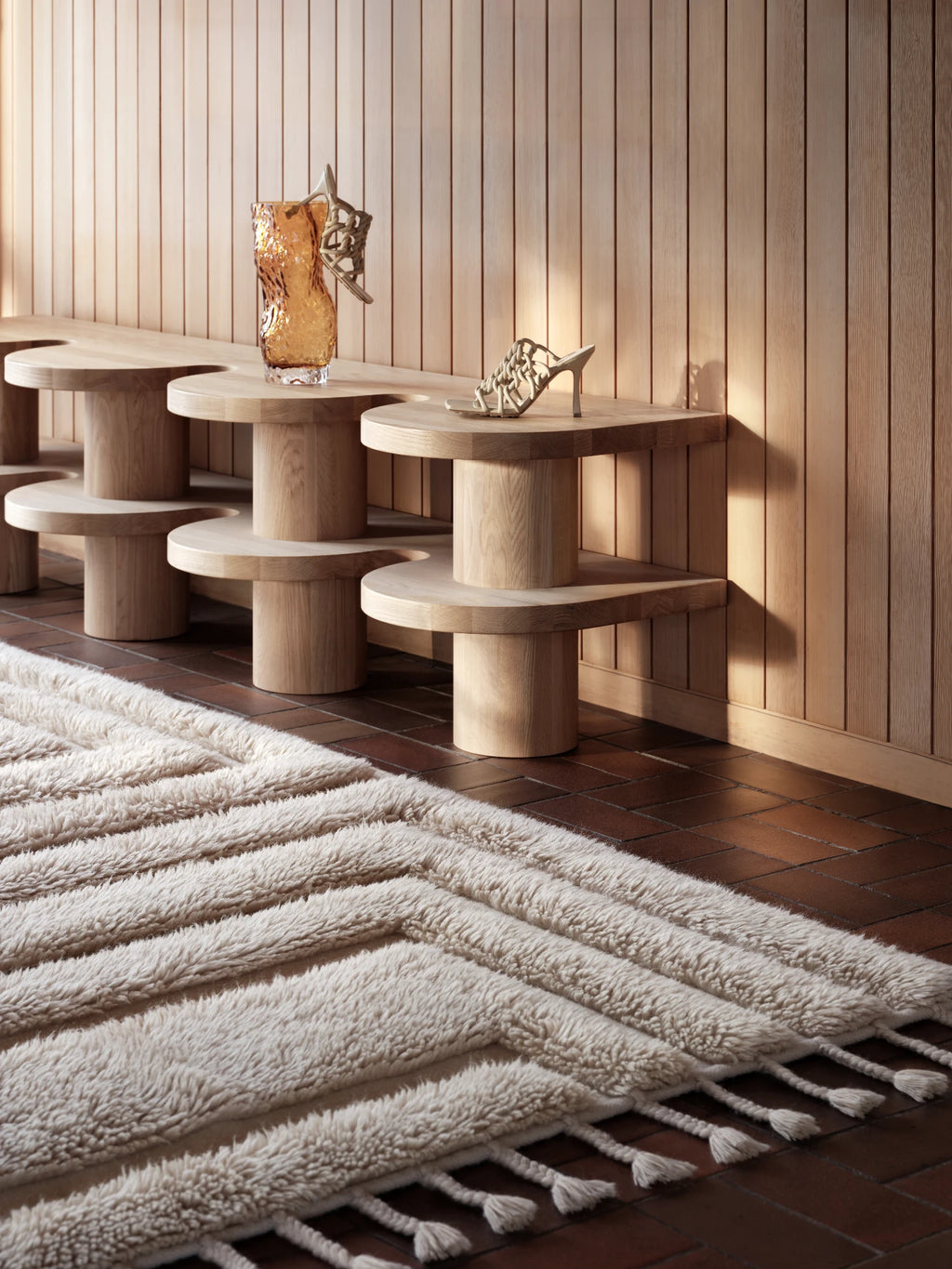 Tinted Objects Kask Wool Rug, a plush off-white textured rug featuring raised horizontal stripes and decorative tassels on the ends, laid on a dark tiled floor. This soft and luxurious area rug is perfect for adding warmth and sophisticated texture to a modern living room or bedroom.