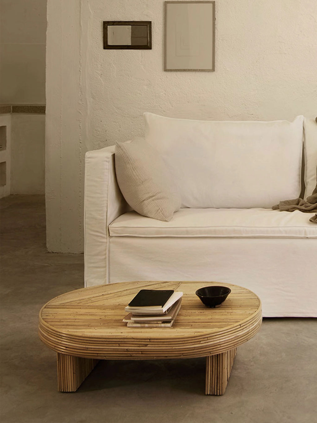 Tine K Viva Rattan Table, an oval natural rattan coffee table with a warm light wood finish, featuring a unique layered and ribbed design crafted from bundled cane sticks for both the tabletop and thick cylindrical legs. This organic modern coffee table is perfect for boho living rooms, coastal interiors, or minimalist spaces seeking a touch of natural texture.