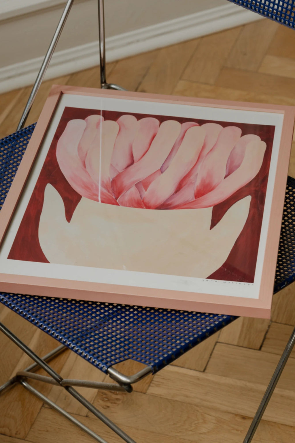The Poster Club Wildrose, an abstract floral art print featuring soft pink, organic petal-like forms held by a cream-colored hand against a deep reddish-brown background, framed in a light.
