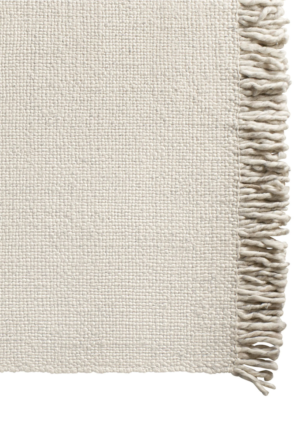 Tine K Sand Wool Rug, a natural hand-woven wool area rug in a soft sand color with a rich, chunky textured weave. It features a dense, off-white pile and a decorative fringe along one edge, providing an organic and inviting aesthetic. This versatile floor covering is perfect for Scandinavian living rooms, minimalist bedrooms, or boho-inspired spaces seeking warmth and natural texture.