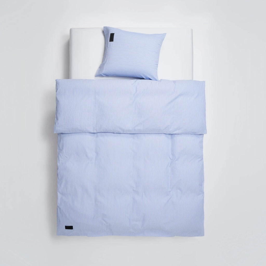 Magniberg Wall Street Duvet Cover - Stripe Light Blue Oxford, a classic pinstripe duvet cover and matching pillowcase crafted from soft Oxford cotton in a serene light blue and crisp white vertical stripe pattern. This minimalist blue bedding set features subtle rumpling for a relaxed yet tailored look, complete with a black brand label accent.