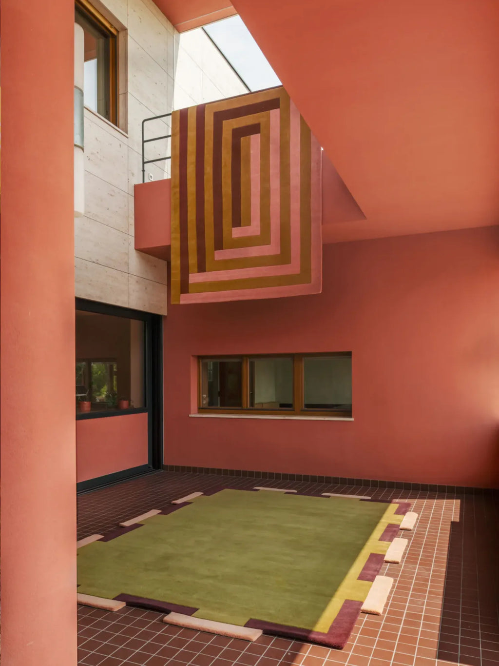 Layered Fregio Wool Rug, a modern green and burgundy geometric patterned area rug with rectangular shapes, laid on a tiled patio. Perfect for adding vibrant color and soft texture to outdoor living...