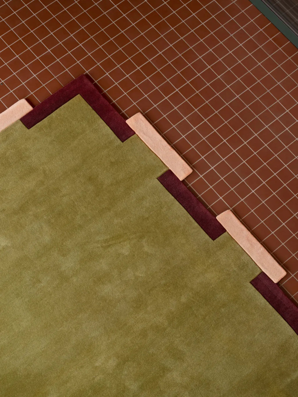 Layered Fregio Wool Rug, a luxurious olive green wool rug with a unique geometric design featuring burgundy and blush pink accents. Perfect for adding a modern, soft touch to any living space or be...