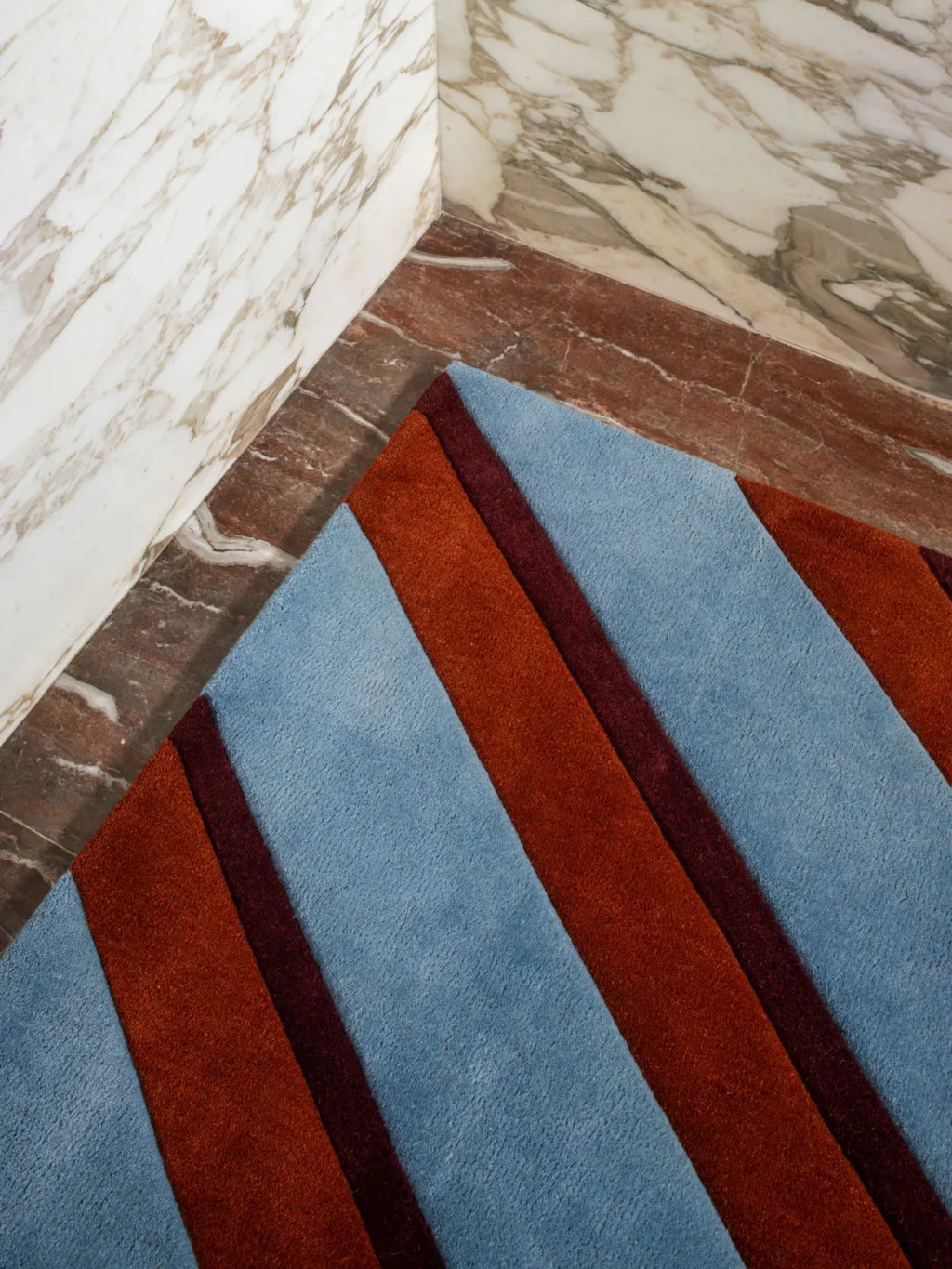Layered Diagonal Wool Rug, a modern wool area rug with alternating diagonal stripes in light blue, burnt orange, and dark burgundy. Perfect for adding a bold contemporary look to living spaces.