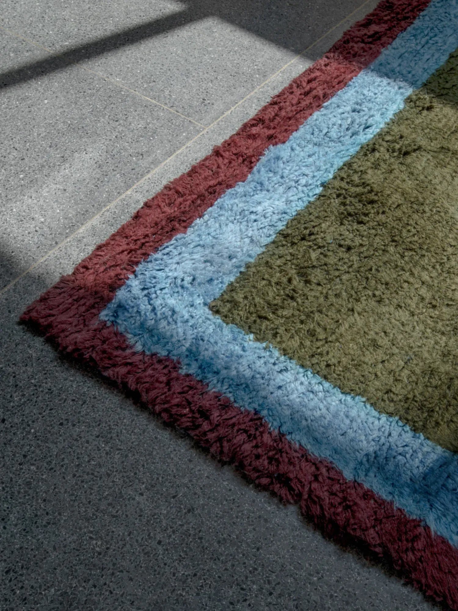Layered Shaggy Edge Wool Rug, a plush, multicolored wool area rug with distinct stripes of deep red, light blue, and olive green. Perfect for adding cozy texture and vibrant color to any living space.