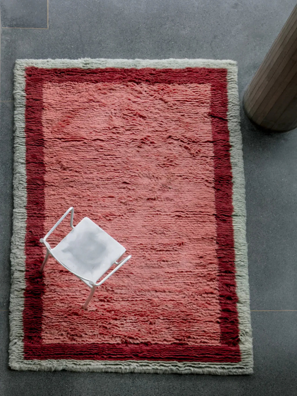 Layered Shaggy Edge Wool Rug, a rectangular, plush, salmon pink wool rug with a contrasting dark red inner border and light grey shaggy outer edges. Perfect for adding warmth and bohemian style to...