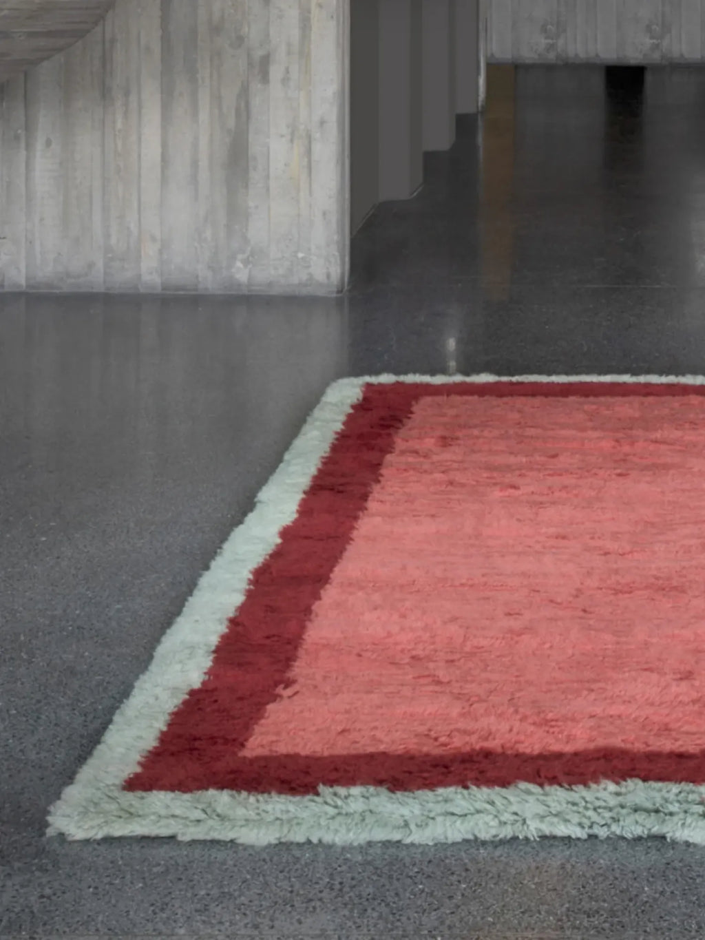 Layered Shaggy Edge Wool Rug, a luxurious coral pink and deep red wool rug with a soft, shaggy texture and light green fringe. Perfect for adding warmth and style to modern living spaces.