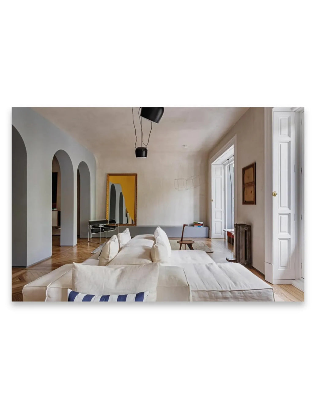 Book World’s Finest Apartments, featuring a spacious, elegant living room with a large white linen sectional sofa, patterned hardwood floors, light gray arched doorways, and a modern gold-framed mirror reflecting a minimalist interior. This inspirational book is perfect for interior design enthusiasts and those seeking luxury living ideas.