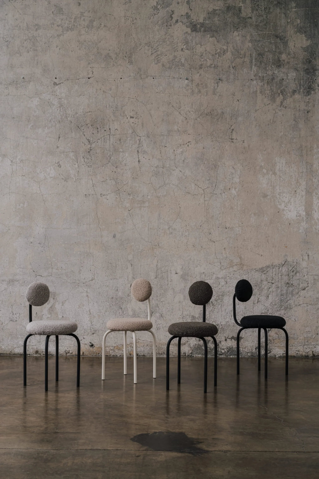 NG DESIGN Object 077 Chairs, a row of four premium contemporary chairs with round bouclé seats and backrests in light grey, beige, dark grey, and black, set on black or white metal bases against a distressed concrete wall. Ideal for minimalist interiors.