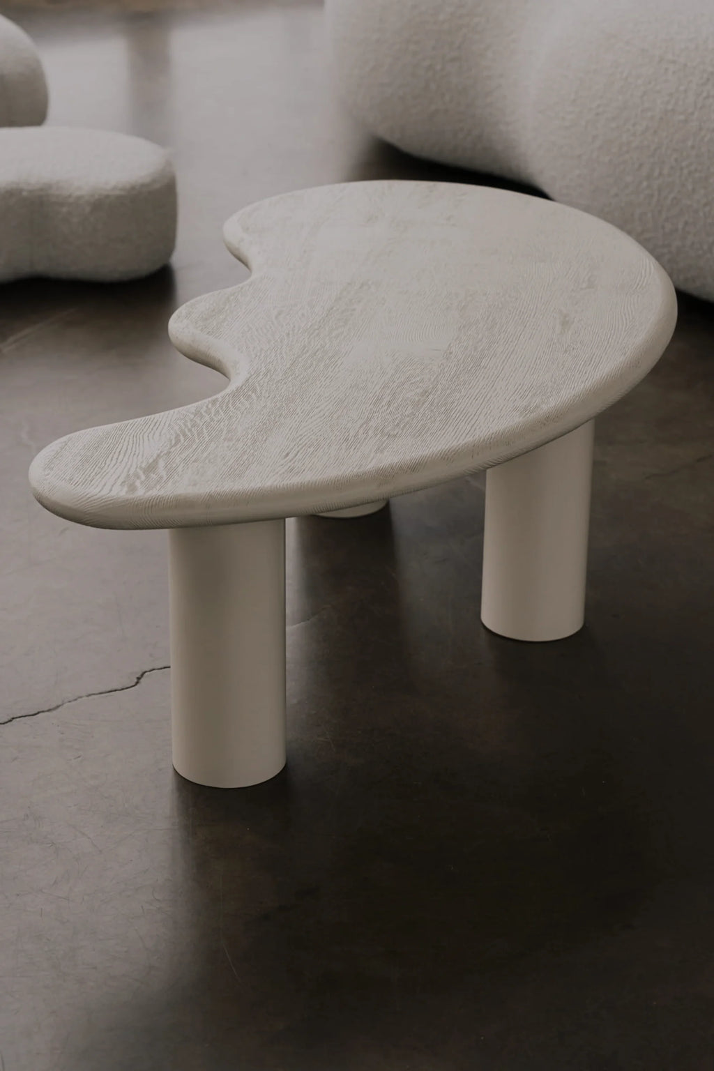 NG DESIGN Object 078 Coffee Table, a modern organic-shaped table with off-white textured woodgrain top and three thick cylindrical legs, displayed on a dark concrete floor. A premium statement piece for luxury living spaces.