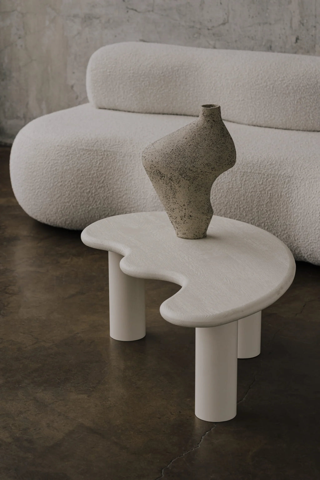 NG DESIGN Object 078 Coffee Table, a modern organic-shaped table with off-white subtly visible wood grain top and three cylindrical legs, styled with an abstract speckled vase, next to a cream boucle sofa. A luxury center piece for any living room.