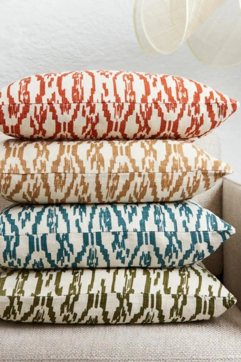 Chhatwal & Jonsson Deccan Linen Throw Pillow, a stack of four rectangular linen throw pillows, each featuring a unique hand-loomed ikat pattern in vibrant colors against a natural off-white background. The global-inspired collection includes rust orange, camel tan, deep teal blue, and olive green cushions, showcasing a rich woven texture. These boho accent pillows are perfect for adding a contemporary touch to living room sofas, bedroom decor, or eclectic home styling.