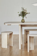 Dining area with a wooden table and stools against a light-colored wall.