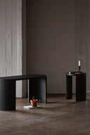 Two black side tables in a minimalistic room with a dark wall and floor.
