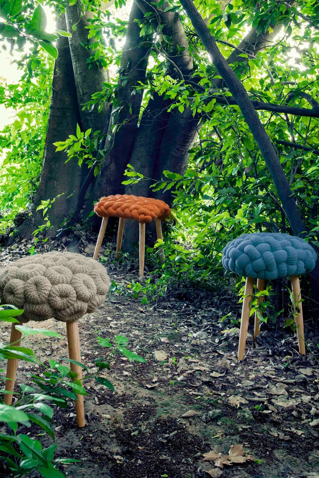 GAN Rugs Knitted Stool, a vibrant collection of organic modern accent stools featuring plush, bulbous hand-knitted seats in textured chunky yarn, available in warm beige, burnt orange, and dusty blue. Each cozy, cloud-like seat is supported by slender, natural solid wood legs, embodying a playful yet sophisticated Scandinavian design. Ideal as versatile accent seating, a footstool, or decorative pouf for contemporary living rooms, cozy bedrooms, or creative children's spaces.