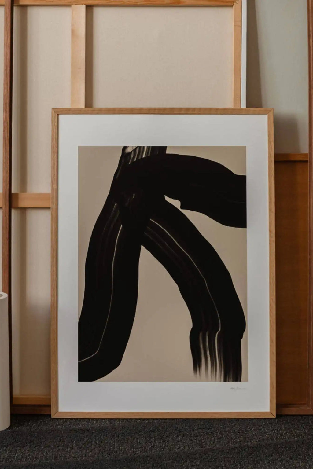 The Poster Club The Walk, a striking abstract art print featuring bold black brushstrokes with textured lines creating an organic, dynamic form against a warm greige background, framed with a clean white mat and a light natural oak frame. This contemporary wall art is ideal for minimalist living rooms, Scandinavian bedrooms, or adding organic modern style to a gallery wall.
