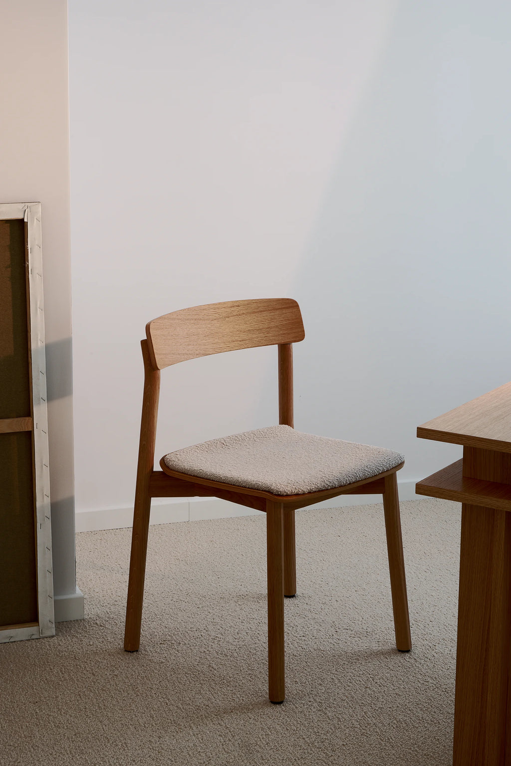 TAMO Arche Chair in a lifestyle setting, showcasing its light brown oak grain wood frame and light beige bouclé upholstered seat. A premium, modern furniture piece. Ideal for stylish dining or office spaces.