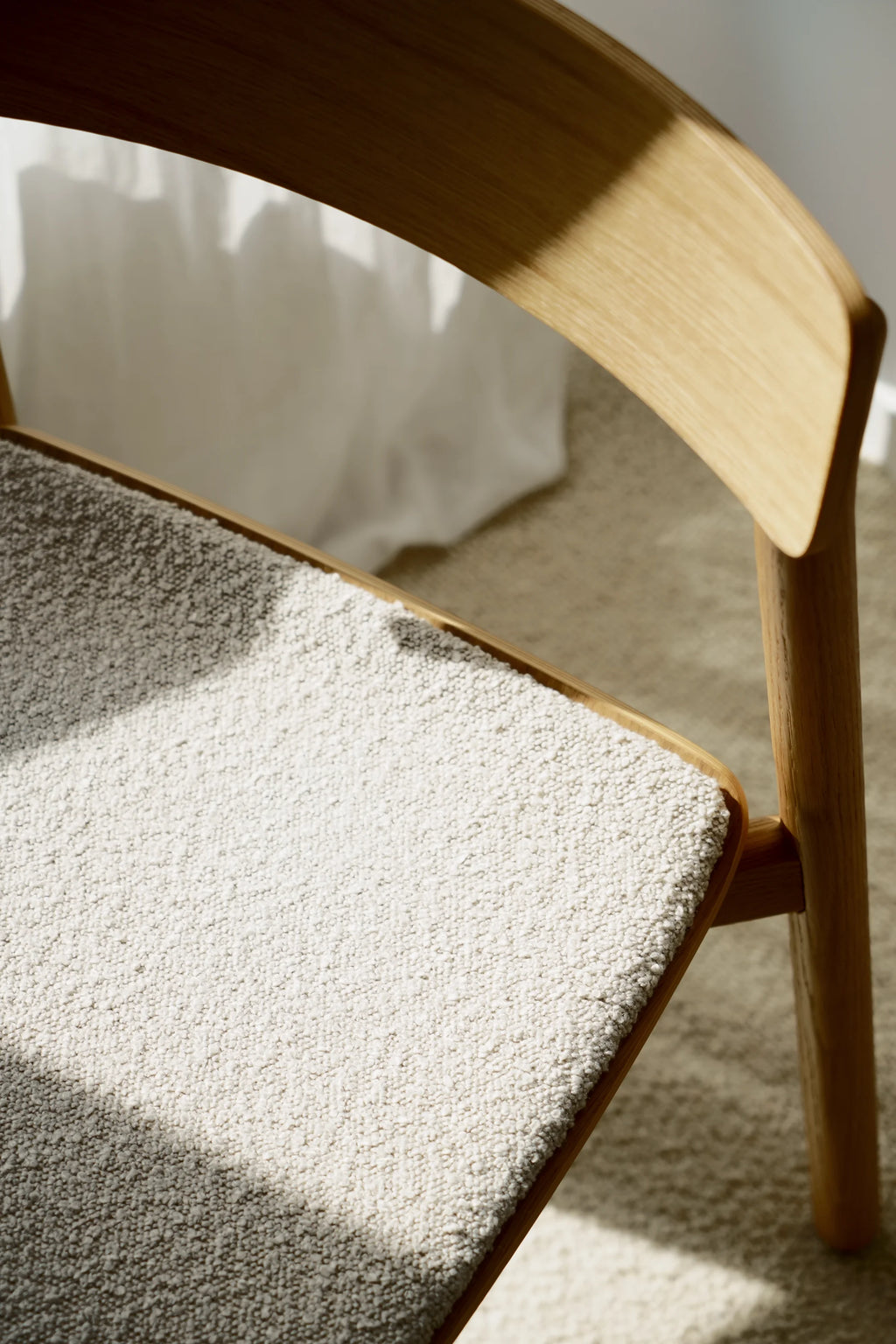 TAMO Arche Chair, a close-up showing light natural oak wood frame and legs with a textured cream-white bouclé fabric seat. Highlighted by sunlight, it's a premium, authentic design. Ideal for modern dining or office spaces.