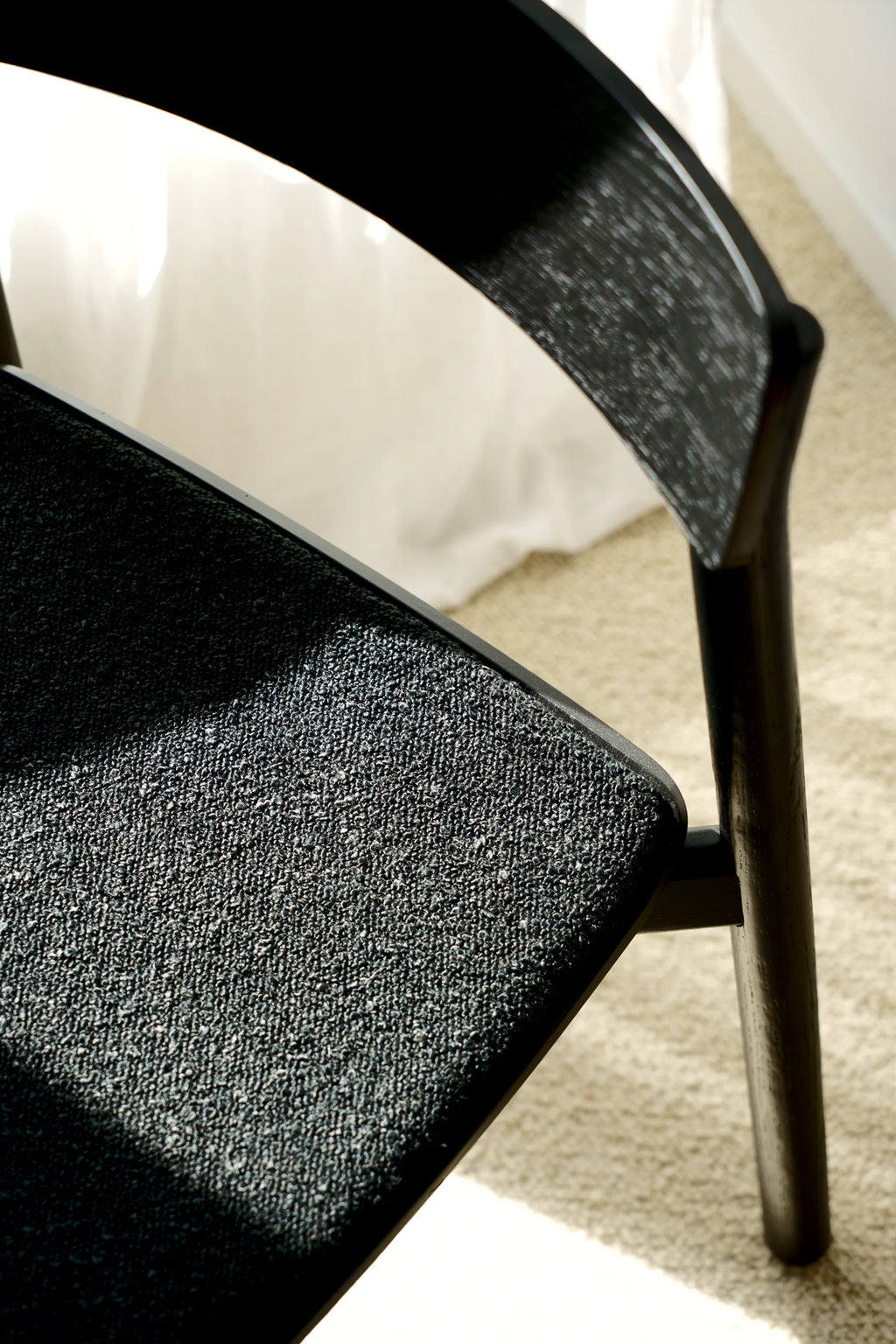 TAMO Arche Chair. Close-up of seat and backrest in textured charcoal gray fabric with dark stained wood curved frame, set against a light rug. A premium dining chair perfect for modern interiors.