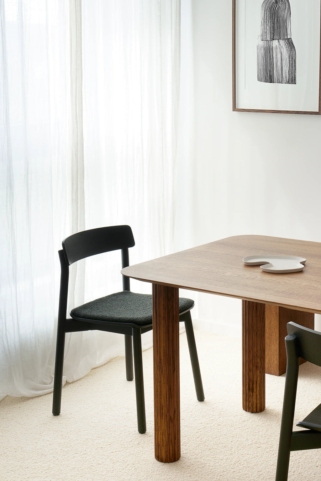 TAMO Arche Chair in a lifestyle setting, featuring a sleek black wooden frame and dark green textured fabric seat, pulled up to a light wood dining table. Ideal for contemporary dining spaces.