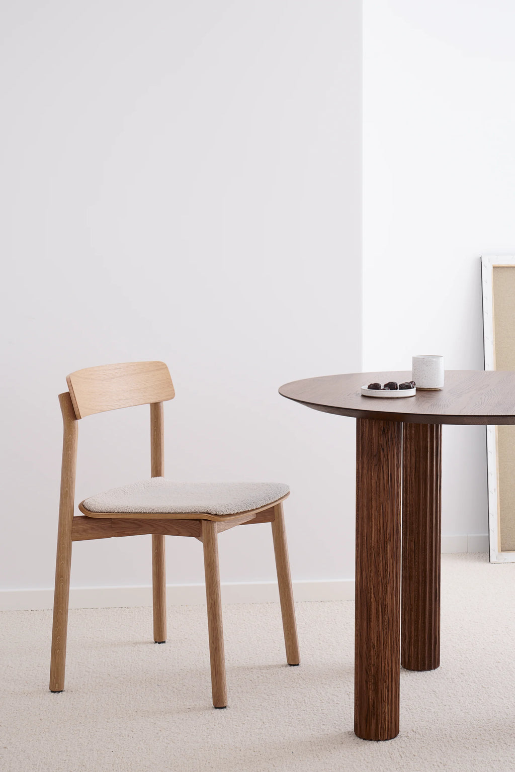 TAMO's Arche Chair, a premium light oak chair with a backrest and cream bouclé upholstered seat, displayed next to a dark wood table. Ideal for modern dining.