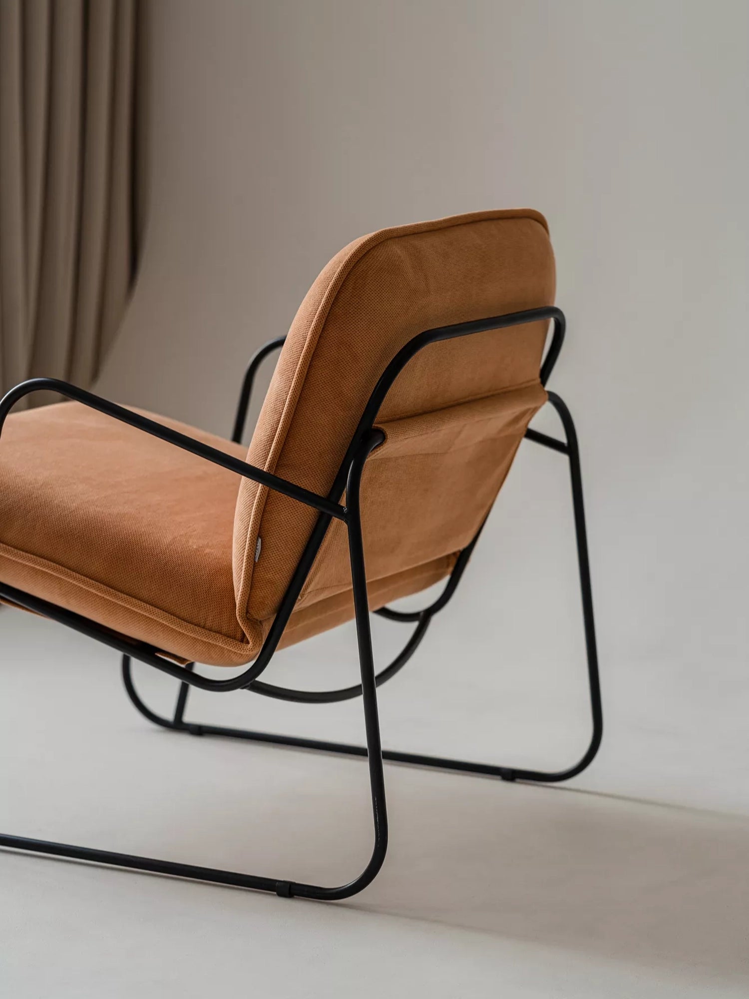 ARTU Tuttu Monteur Armchair, a contemporary lounge chair with a sleek matte black metal frame supporting plush, textured terracotta orange fabric cushions and a coordinating fabric sling back.