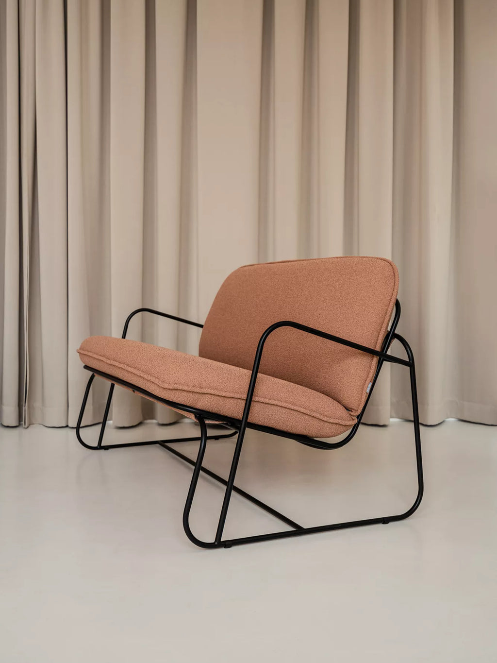 ARTU Tuttu Monteur Sofa, a contemporary lounge sofa featuring a continuous matte black tubular metal frame with plush, removable cushions upholstered in a warm terracotta-toned textured fabric.