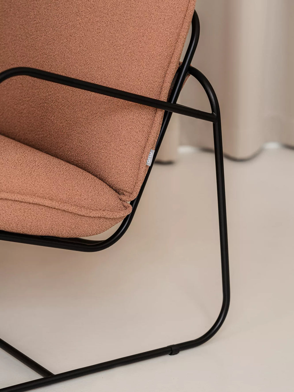 ARTU Tuttu Monteur Sofa, a modern minimalist sofa featuring a sleek matte black tubular steel frame with continuous curves, upholstered in a warm terracotta-toned textured woven fabric.