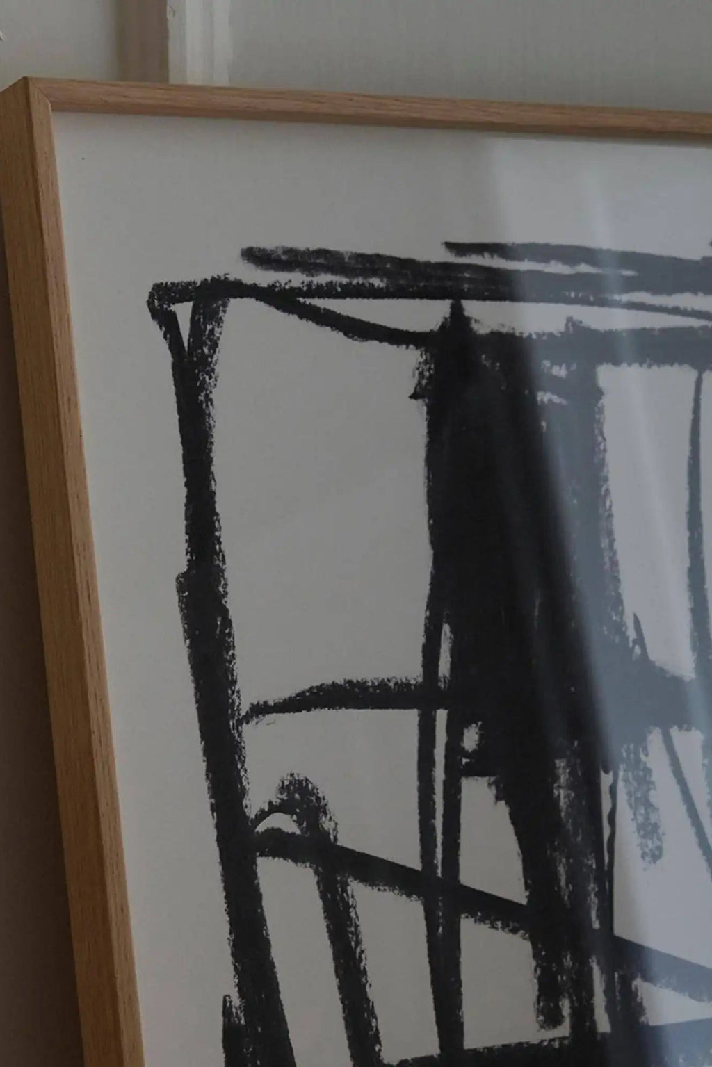 The Poster Club Turmoil, an expressive abstract art print featuring bold, textured black charcoal-like strokes on a clean white background, framed in a light natural oak frame. This modern minimalist wall art is perfect for creating a focal point in contemporary living rooms, bedrooms, or gallery walls.