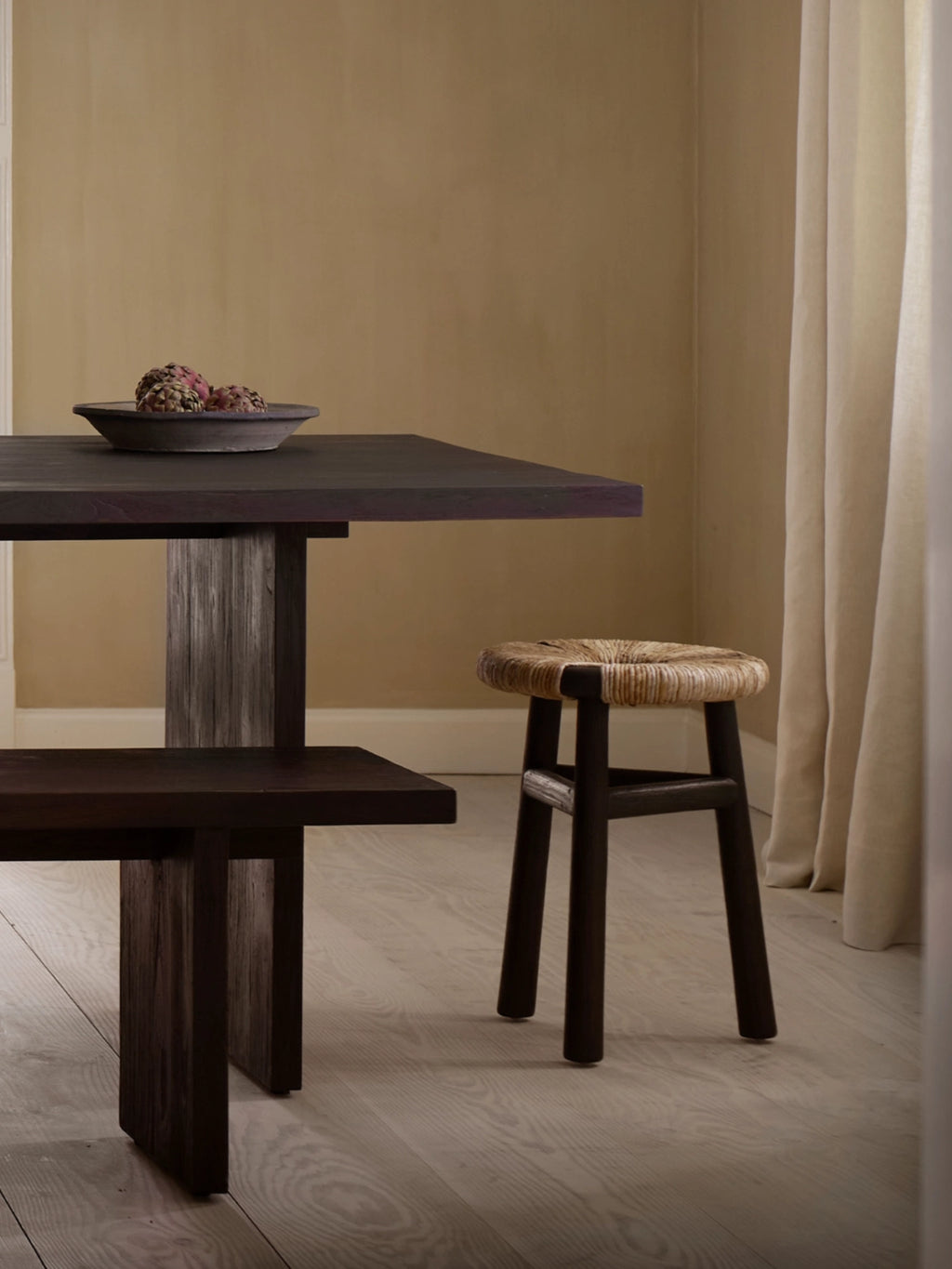 Tine K Kayu Stool, an organic modern accent stool featuring a sturdy dark brown solid wood frame with a round, hand-woven natural fiber seat in a rustic beige texture. This versatile stool is perfect as a stylish side table or additional seating in minimalist living rooms, Japandi bedrooms, or wabi-sabi inspired spaces.