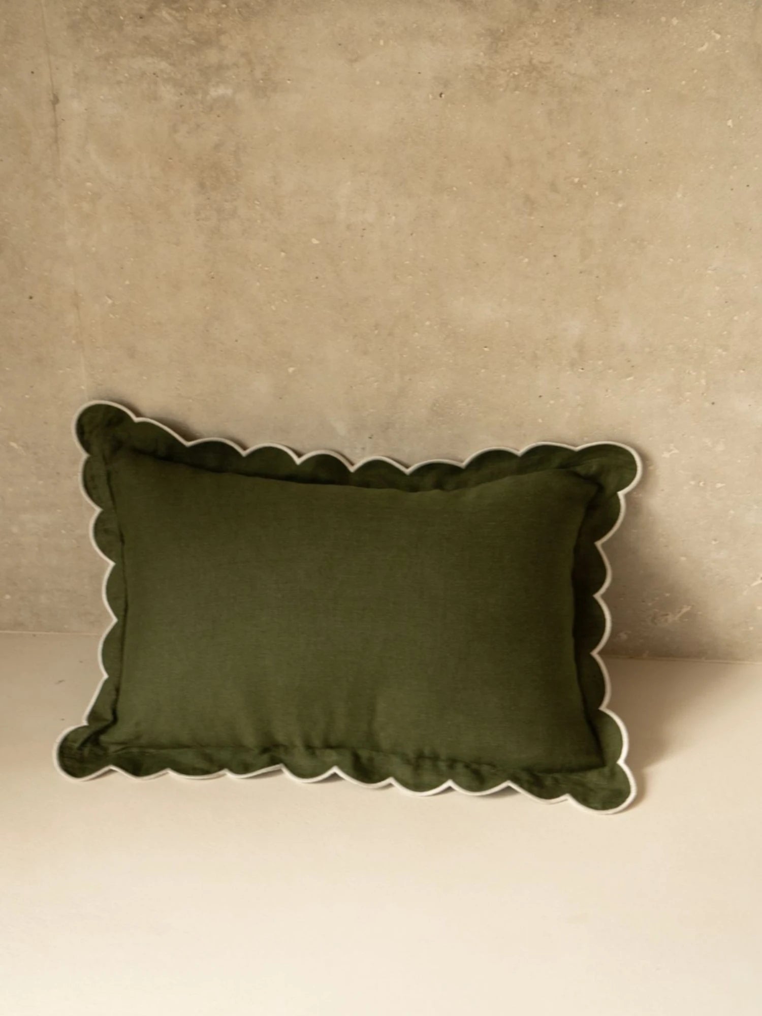 Green pillow with scalloped edge on a beige background